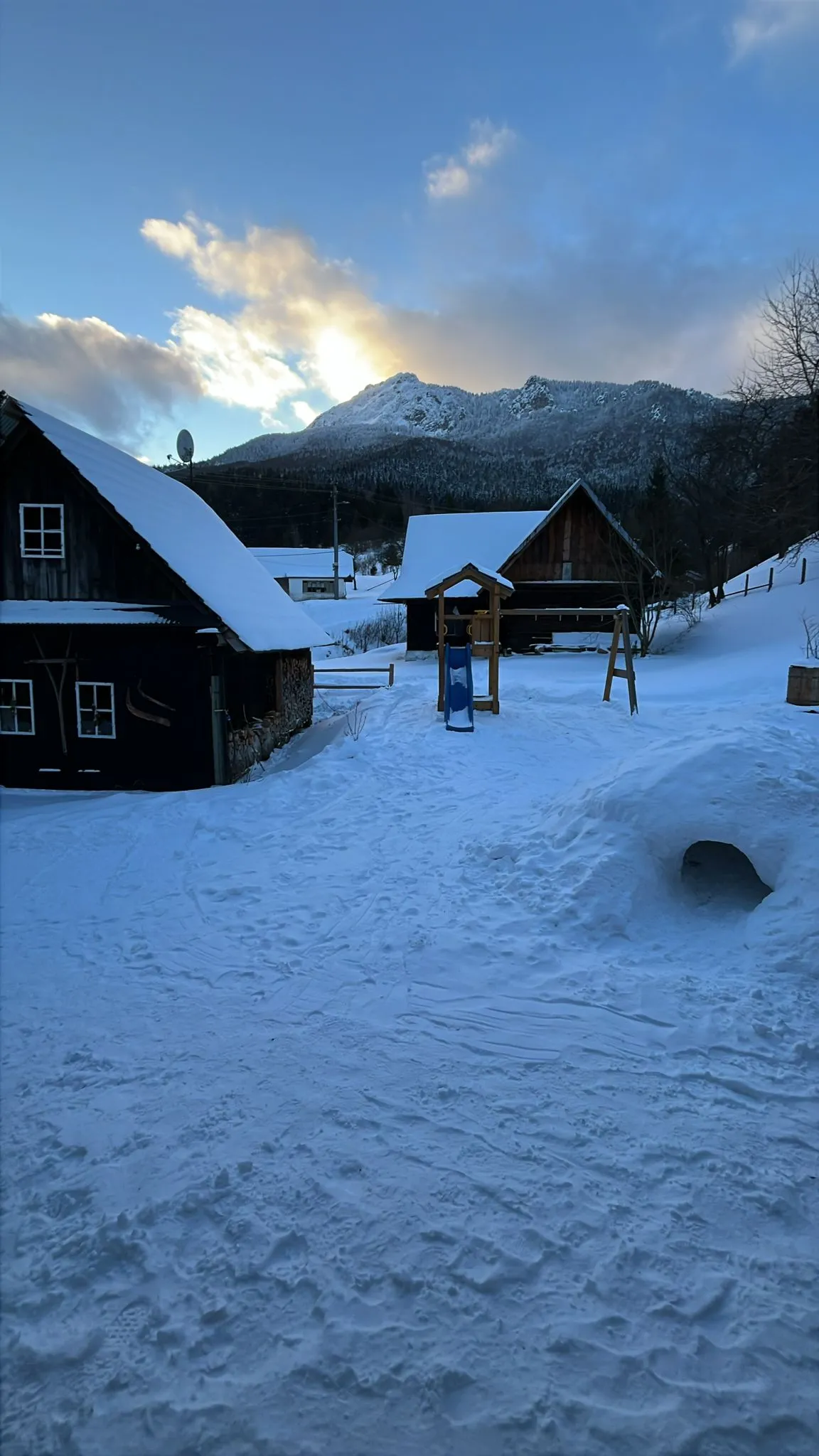 Ośnieżone drewniane chaty i plac zabaw w złotym świetle pod górami Małej Fatry.