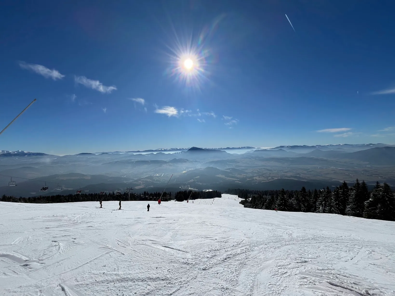 Lyžiari na zasneženom svahu s lanovkou a panoramatickým výhľadom na pohoria